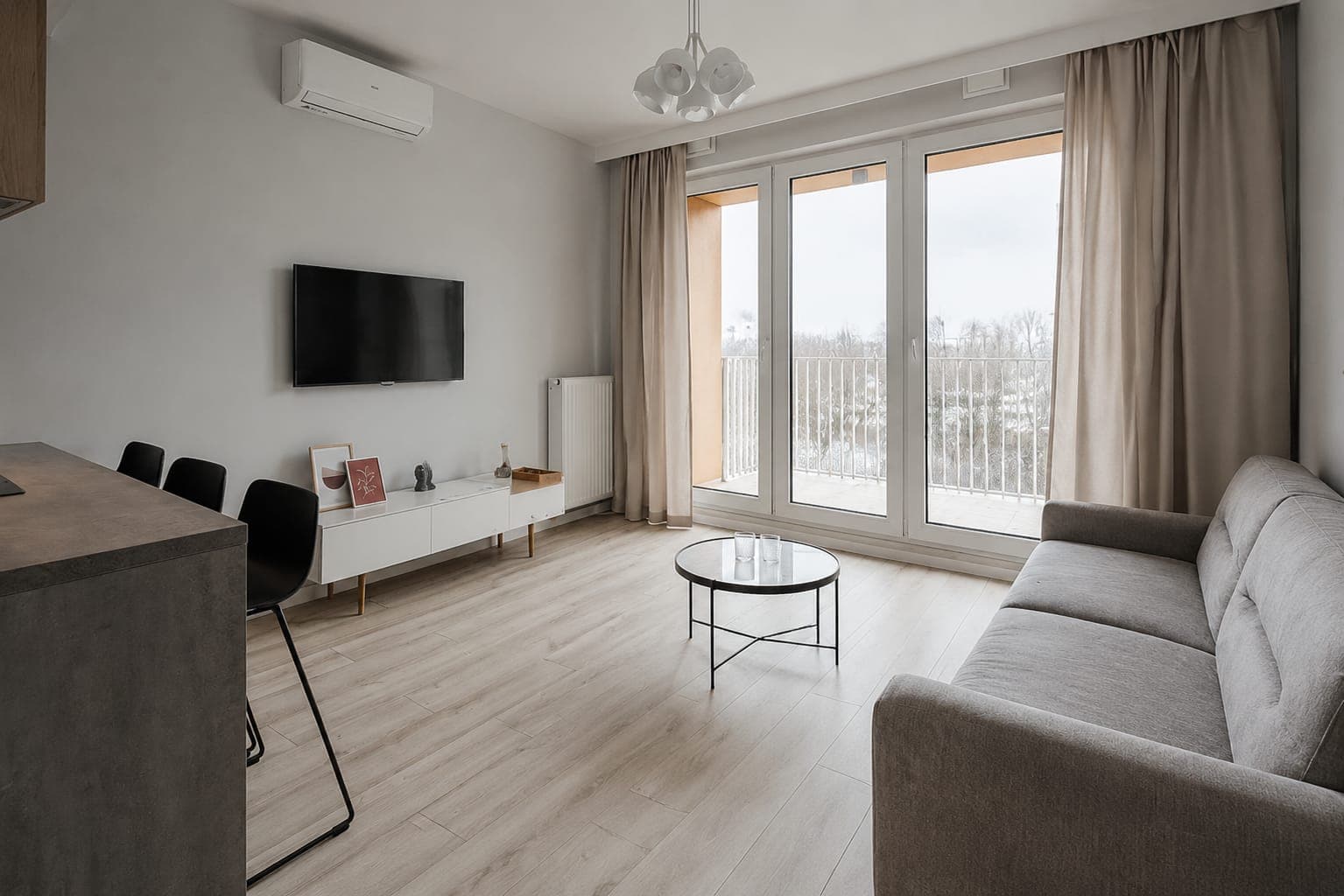 Pale living room with a grey sofa and glass onto the balcony, apartment on Aignera in Ursynów, Warsaw